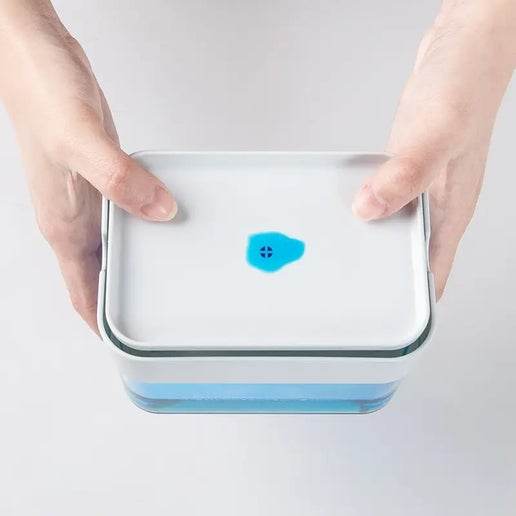 Hands holding a rectangular Soap Dispenser with blue Soap on a white background