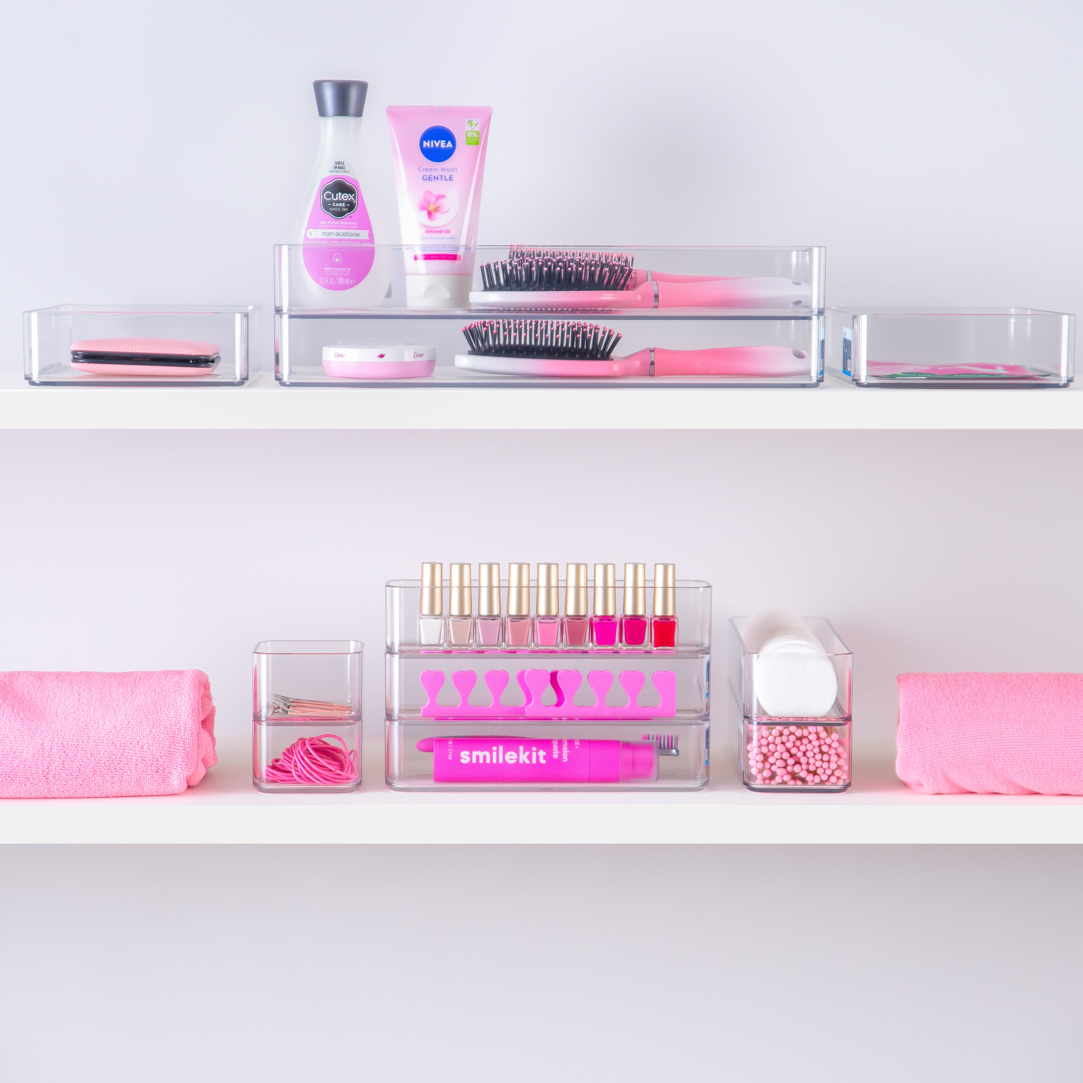Bathroom shelf with pink and white toiletries in clear organiser containers on a light gray background