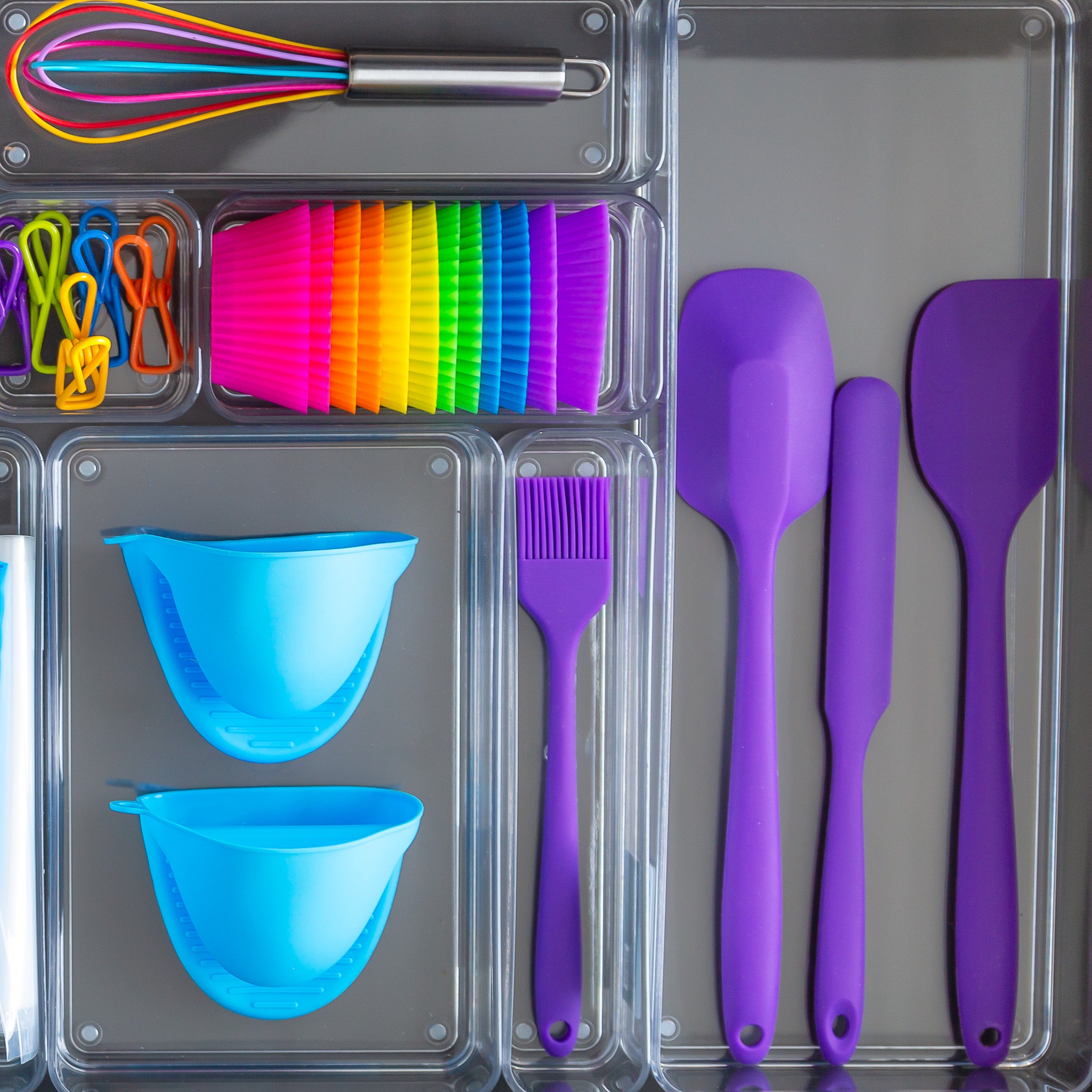 Set of colorful kitchen utensils including spatulas, bowls, and a whisk in clear organizers.