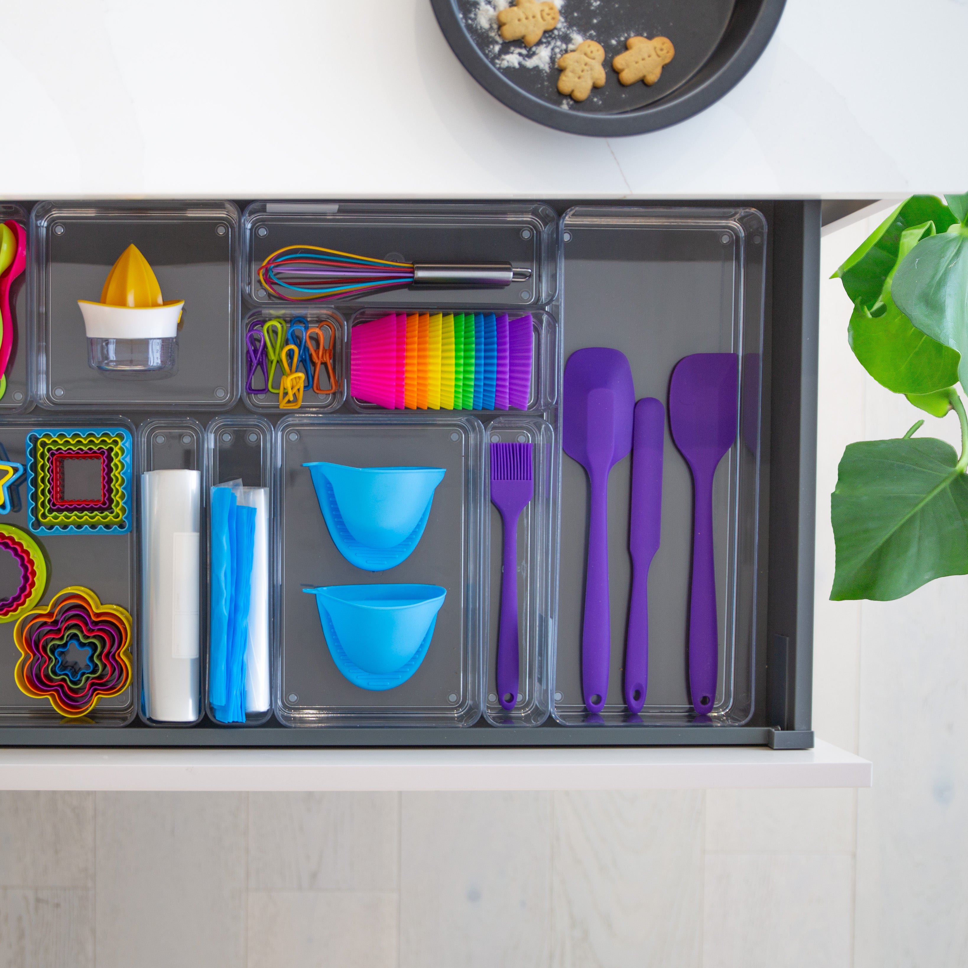 Colorful kitchen utensils and tools in a drawer in drawer organisers, with a plant in the background