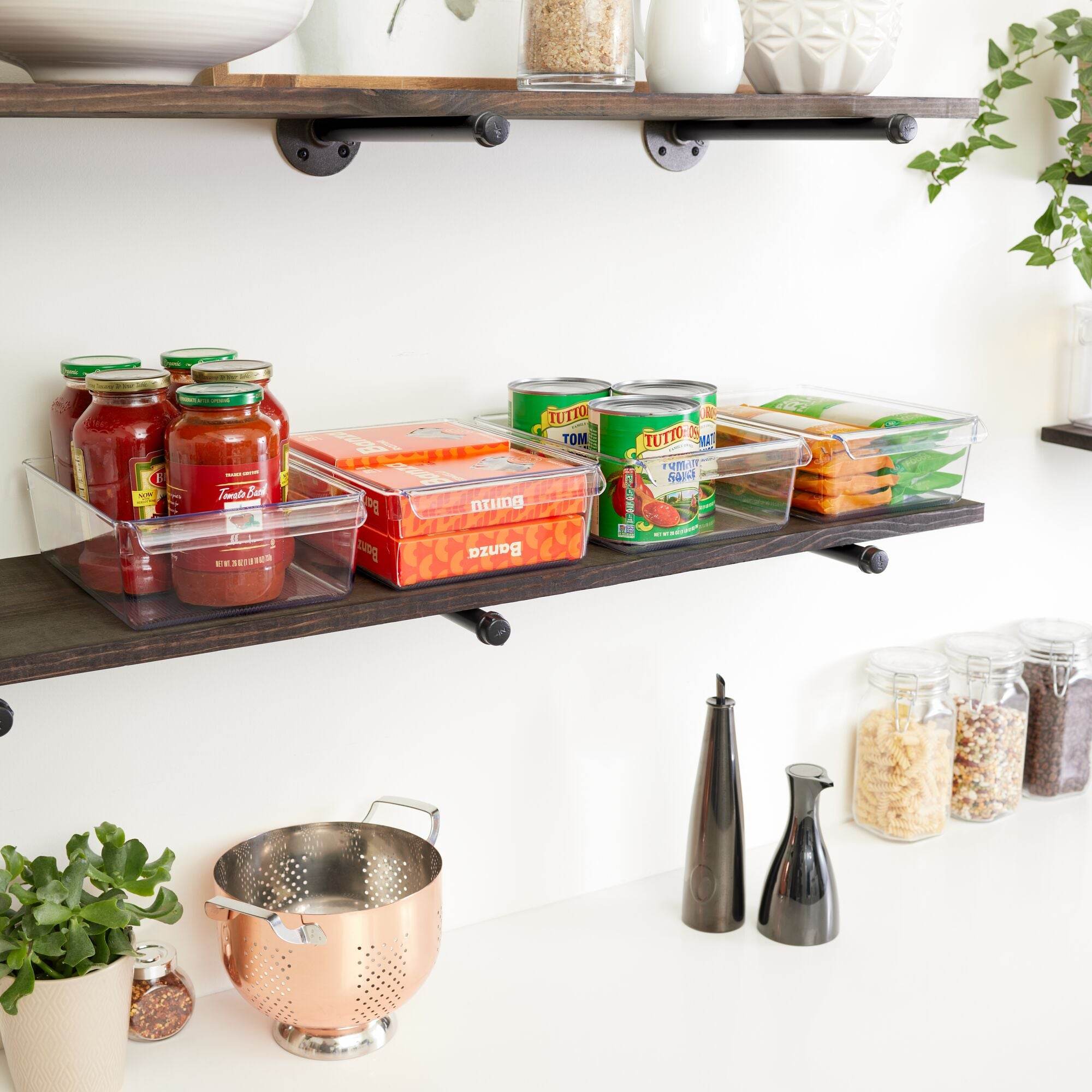 Kitchen shelves with iDesign food containers, a colander, and kitchen utensils on a white countertop.