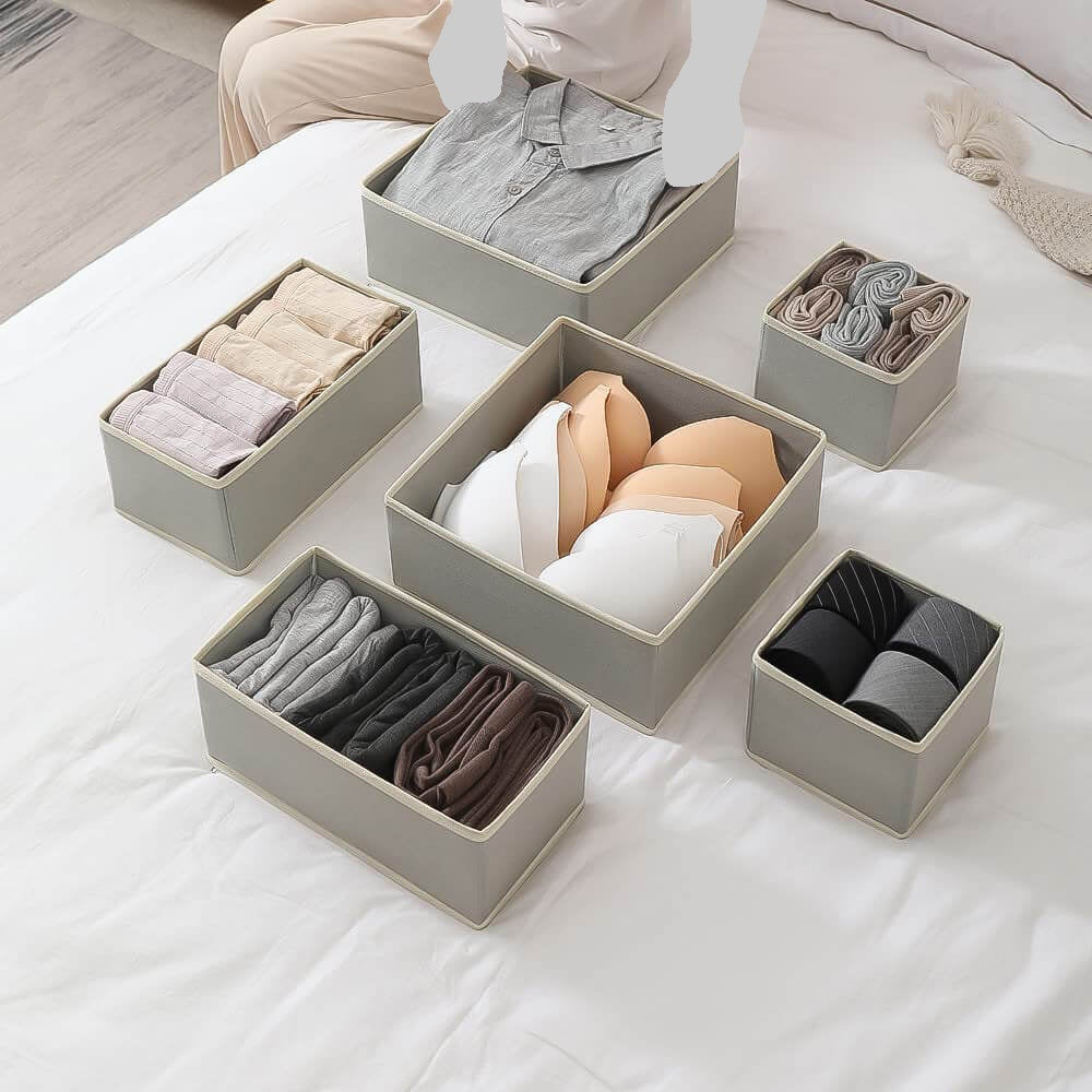 Set of gray storage boxes on a bed containing folded clothes.