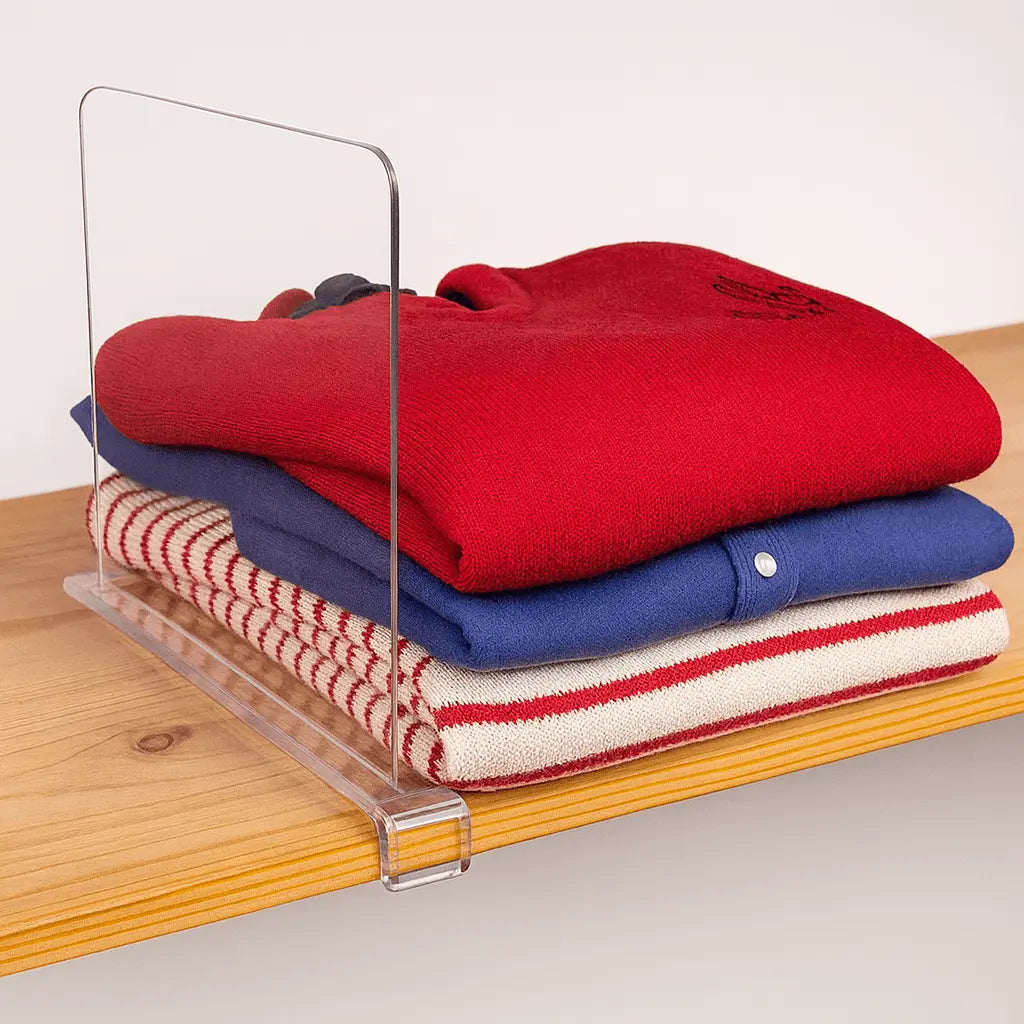 Stack of folded sweaters on a clear acrylic shelf against a white background