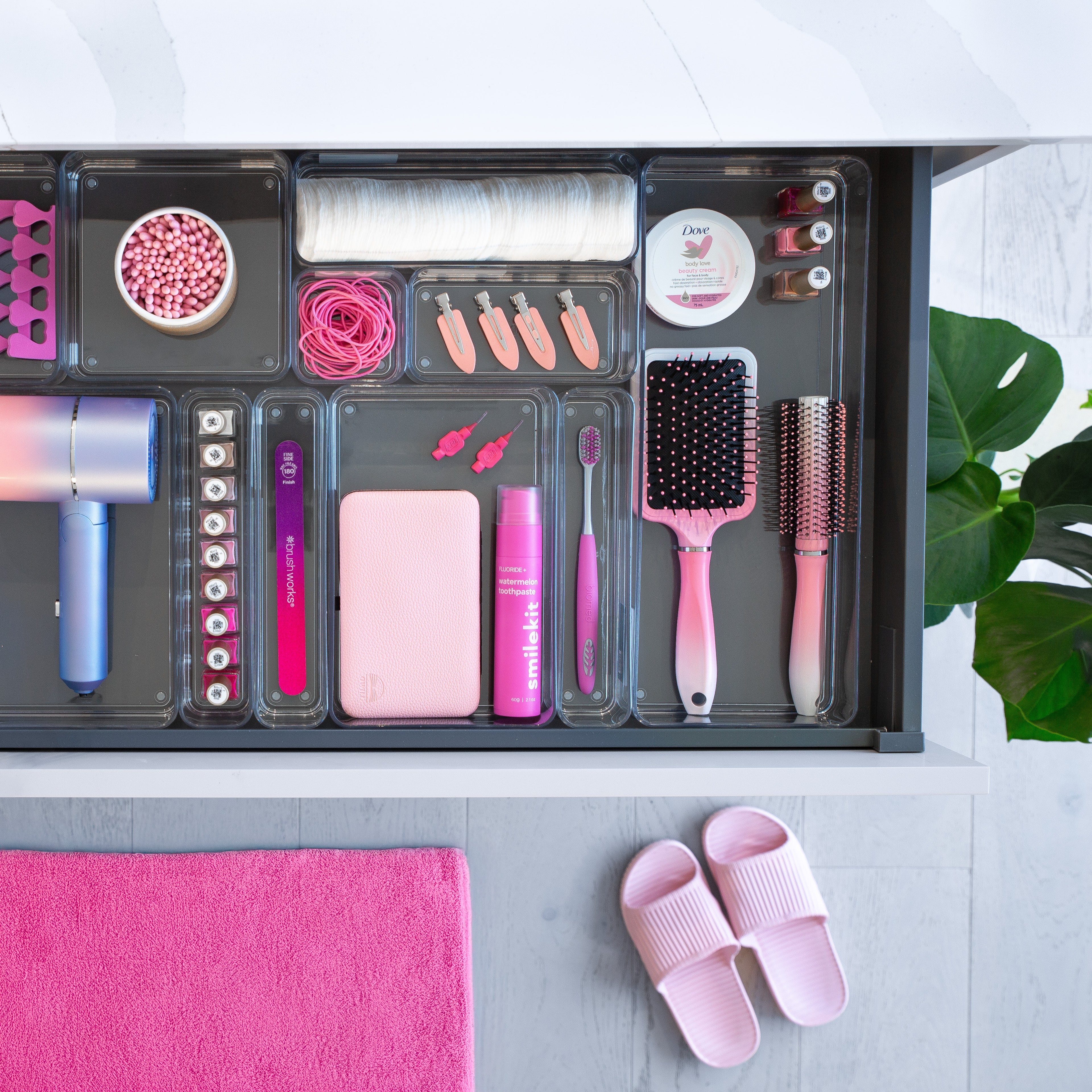 Collection of pink hair care products and tools in clear drawer organisers with a plant in the background.
