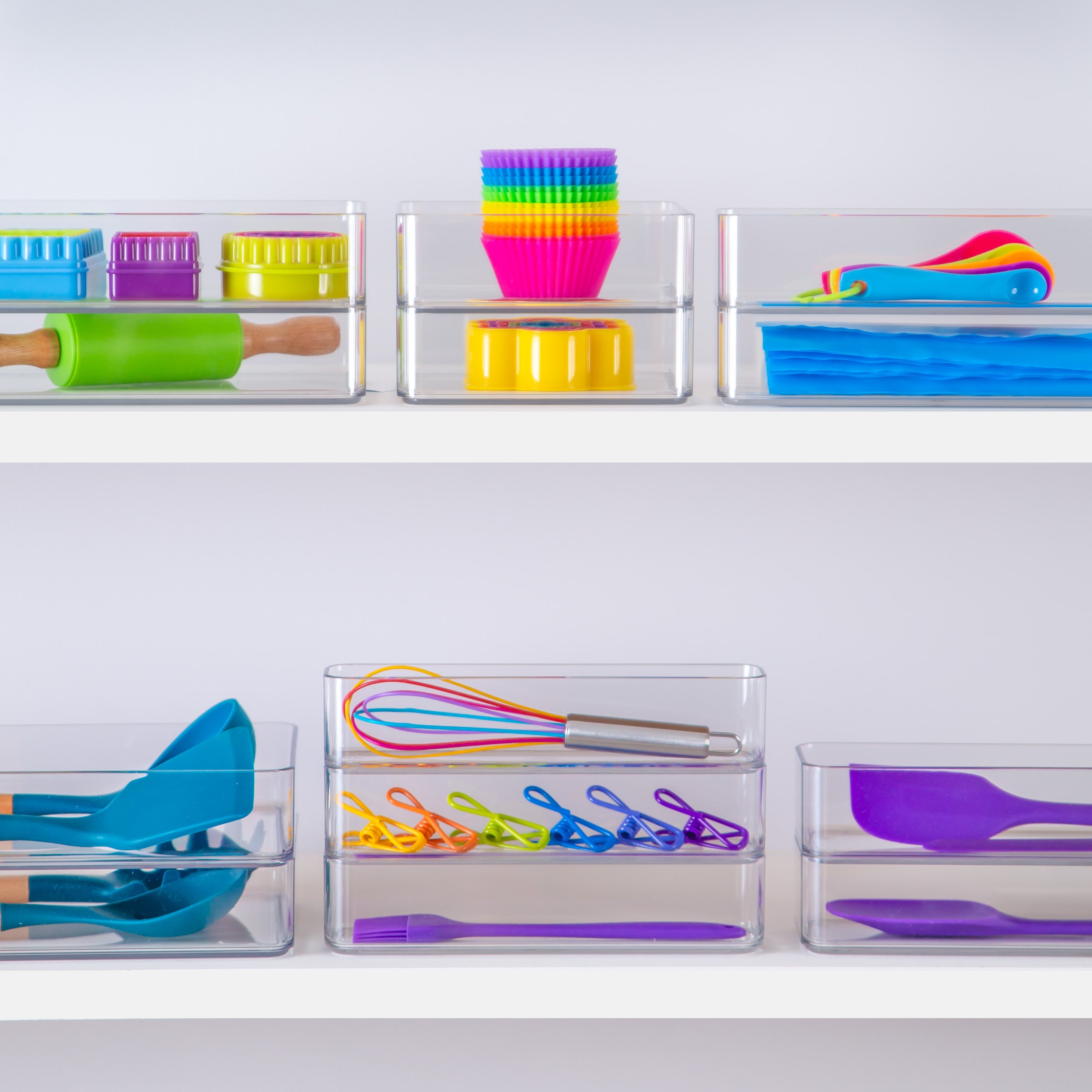 Colorful kitchen utensils in transparent drawer inserts on a white shelf