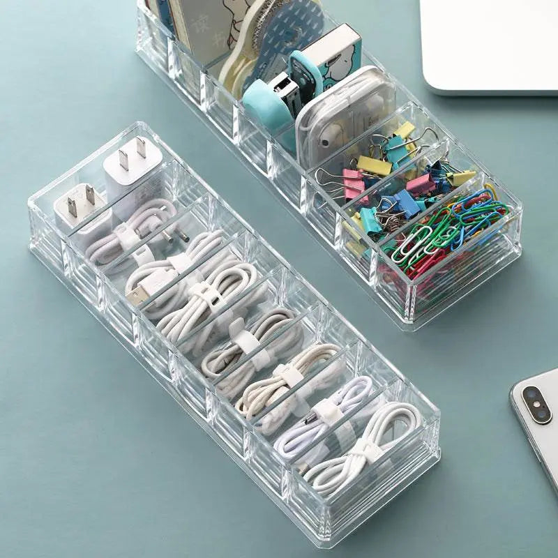 Clear  desk organizer with compartments for cables, clips, and office supplies on a light blue surface.